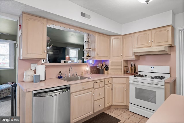 kitchen featuring light brown cabinets, gas range gas stove, under cabinet range hood, dishwasher, and a sink