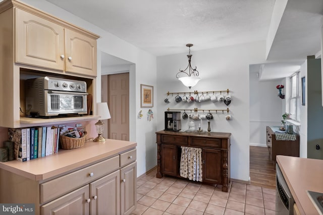 kitchen featuring light countertops, light tile patterned floors, baseboards, dishwasher, and hanging light fixtures