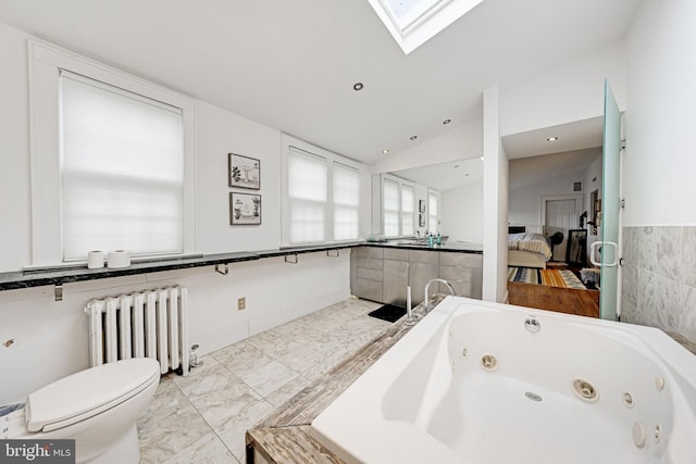 bathroom with radiator, lofted ceiling with skylight, a jetted tub, toilet, and marble finish floor