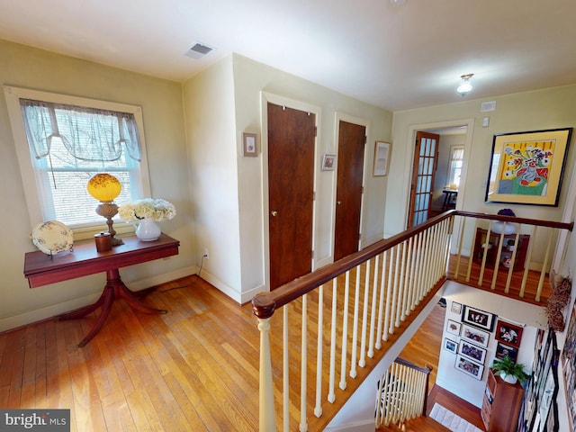 corridor featuring an upstairs landing, visible vents, baseboards, and wood-type flooring