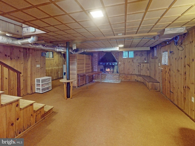 below grade area featuring carpet floors, wooden walls, a brick fireplace, and water heater