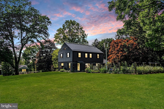 view of front of house featuring fence, a standing seam roof, a front lawn, stone siding, and metal roof