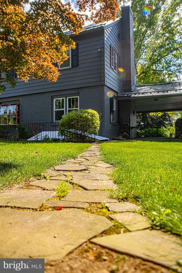 view of side of property featuring brick siding, a chimney, and a yard