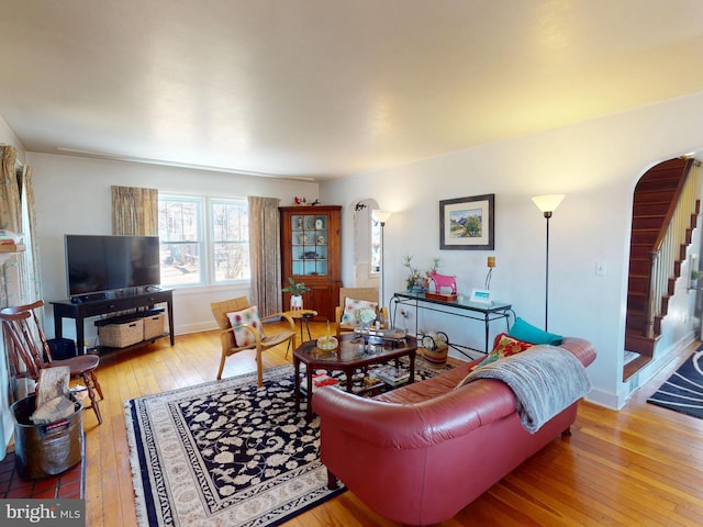 living room featuring arched walkways, stairway, baseboards, and hardwood / wood-style flooring