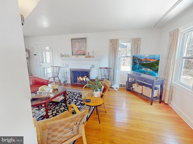 living room with visible vents, a warm lit fireplace, hardwood / wood-style floors, and a healthy amount of sunlight