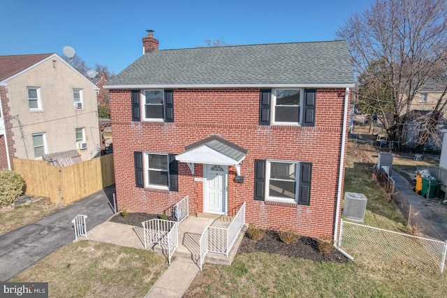 view of front of property with central air condition unit, brick siding, fence private yard, and a chimney