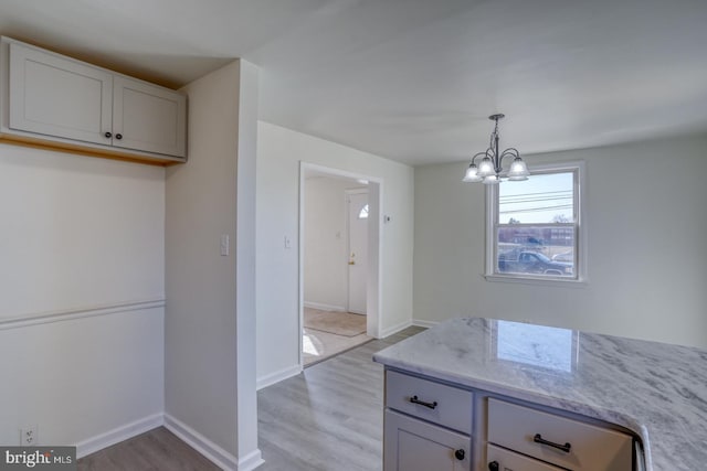 kitchen featuring light stone countertops, baseboards, an inviting chandelier, pendant lighting, and light wood-type flooring