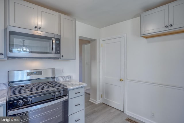 kitchen featuring white cabinetry, light stone counters, light wood-style floors, and appliances with stainless steel finishes