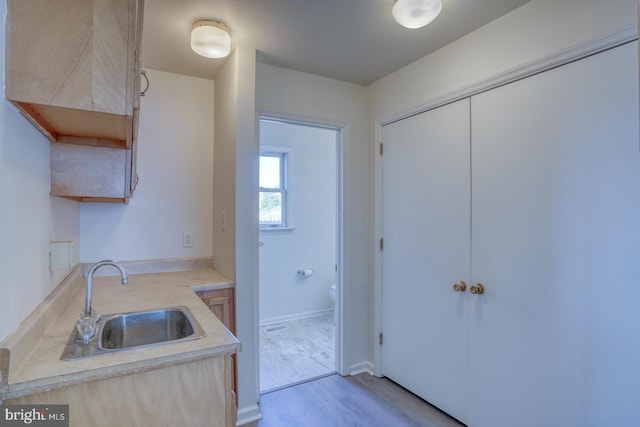 kitchen featuring a sink, baseboards, light wood finished floors, and light countertops