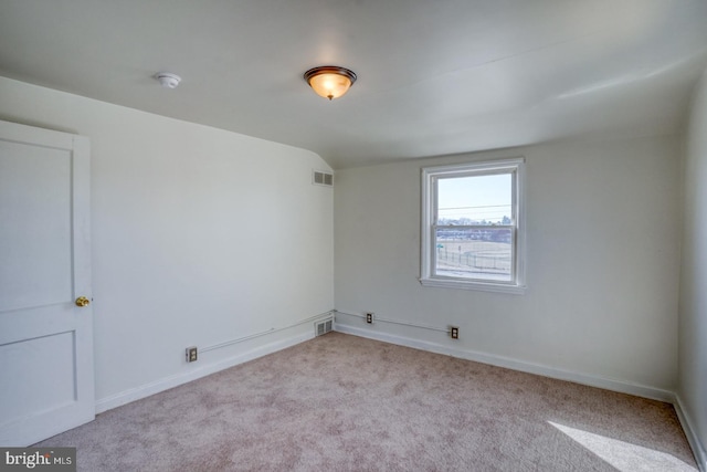 carpeted spare room featuring visible vents, baseboards, and lofted ceiling