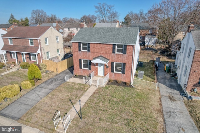 view of front of house with fence, driveway, roof with shingles, a front lawn, and brick siding