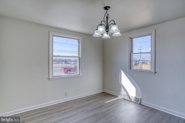 unfurnished room featuring a notable chandelier, wood finished floors, and baseboards