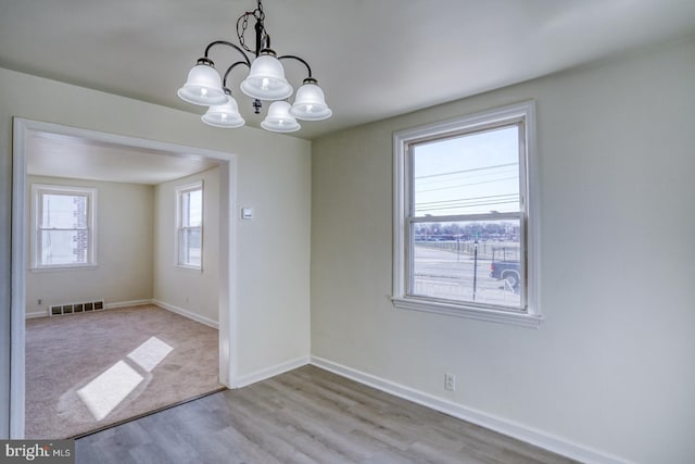 unfurnished room with a notable chandelier, visible vents, baseboards, and wood finished floors