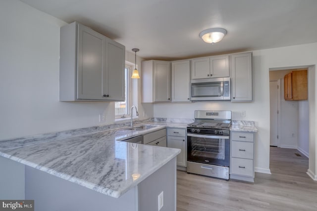 kitchen with light stone countertops, light wood finished floors, a peninsula, a sink, and appliances with stainless steel finishes