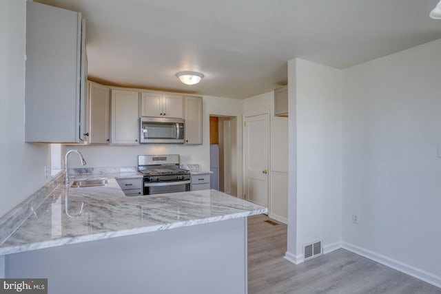 kitchen with visible vents, light stone countertops, light wood-type flooring, stainless steel appliances, and a sink