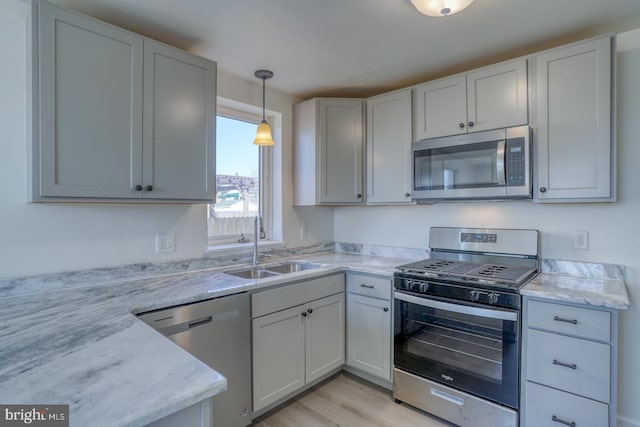 kitchen with a sink, decorative light fixtures, appliances with stainless steel finishes, light wood finished floors, and light stone countertops