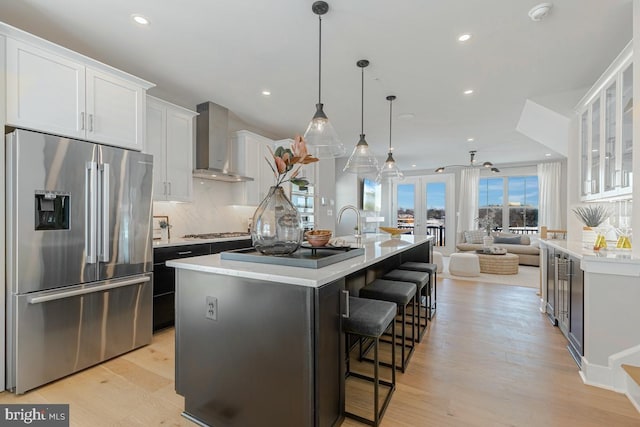 kitchen featuring light wood-style flooring, stainless steel appliances, decorative backsplash, white cabinetry, and wall chimney range hood