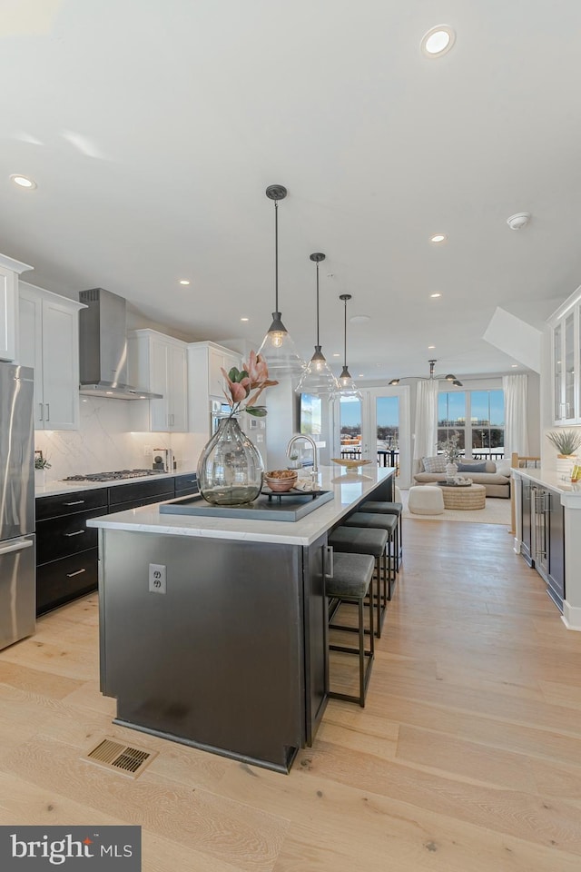 kitchen with a spacious island, light wood-type flooring, appliances with stainless steel finishes, white cabinetry, and wall chimney exhaust hood