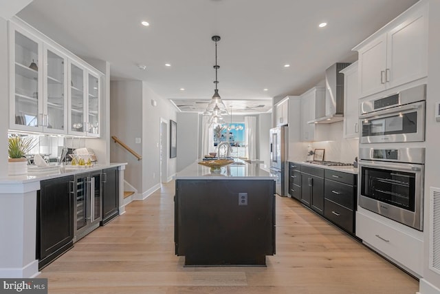 kitchen featuring white cabinets, wall chimney exhaust hood, light wood-style floors, and appliances with stainless steel finishes