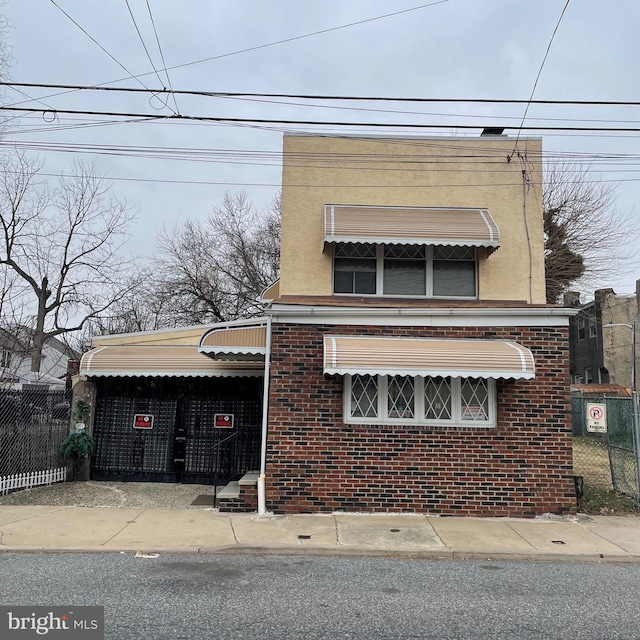 view of front of house with stucco siding, an attached carport, brick siding, and fence