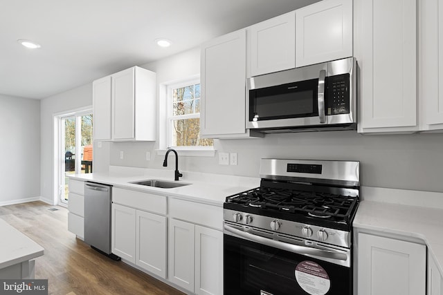 kitchen with wood finished floors, recessed lighting, a sink, stainless steel appliances, and white cabinets