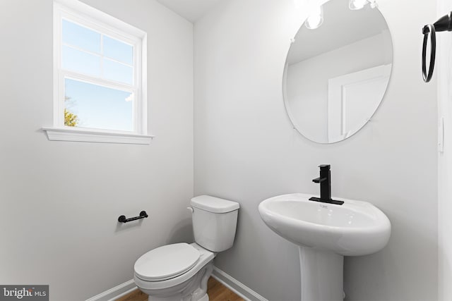 half bath with a sink, toilet, baseboards, and wood finished floors