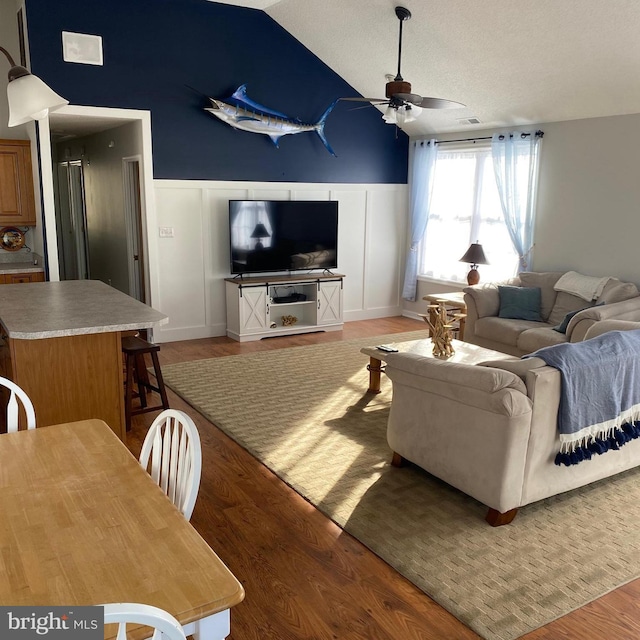 living area featuring light wood-type flooring, visible vents, a wainscoted wall, a ceiling fan, and lofted ceiling