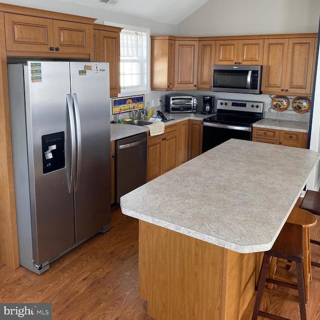 kitchen with stainless steel appliances, lofted ceiling, and brown cabinetry