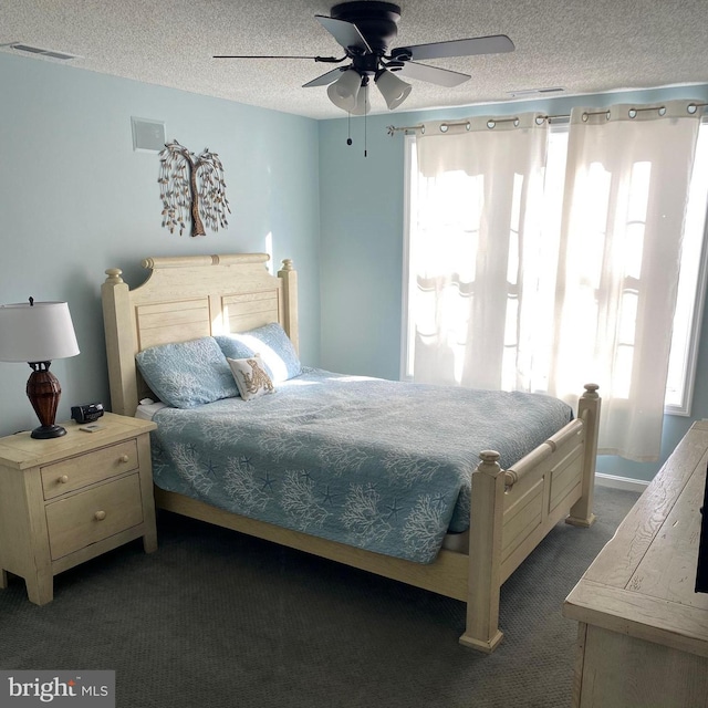 bedroom with dark colored carpet, visible vents, a textured ceiling, and a ceiling fan