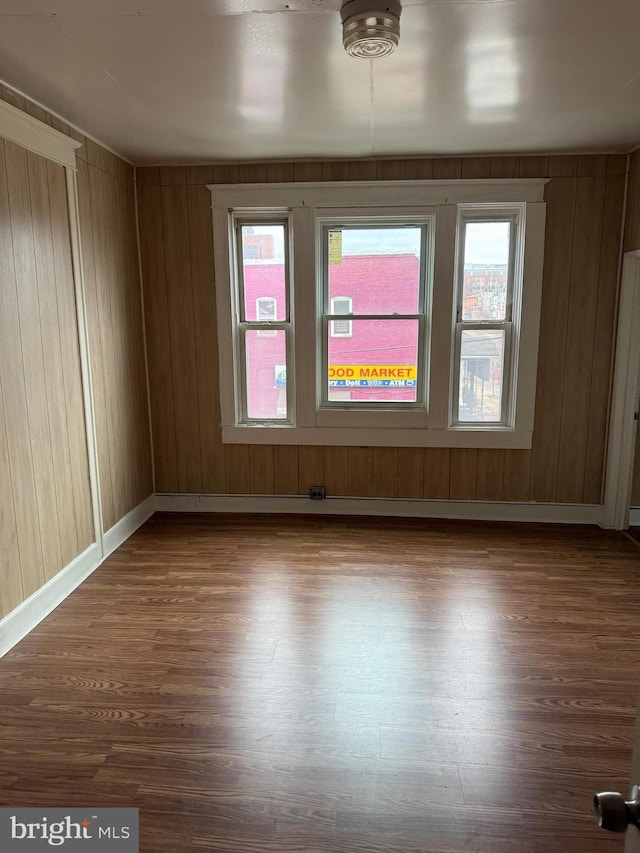 unfurnished room with wood walls, dark wood-type flooring, and baseboards