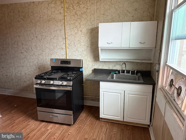 kitchen with dark countertops, wallpapered walls, light wood-style flooring, stainless steel gas stove, and a sink