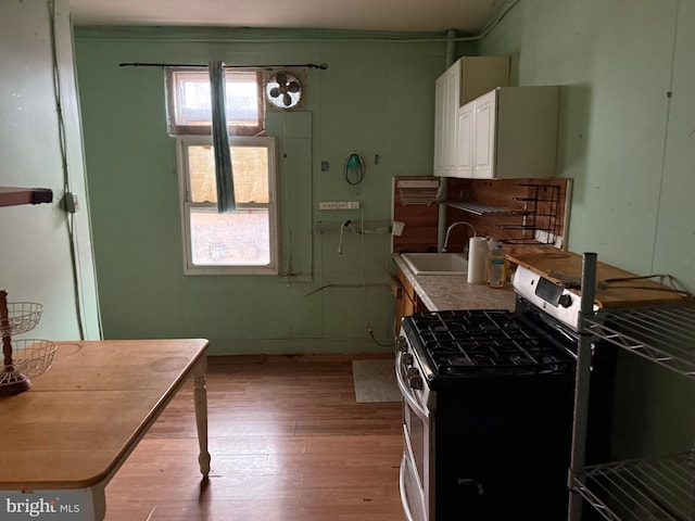 kitchen featuring stainless steel gas range oven, light countertops, light wood-type flooring, white cabinets, and a sink