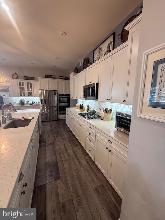 kitchen featuring dark wood finished floors, decorative backsplash, white cabinets, stainless steel appliances, and a sink