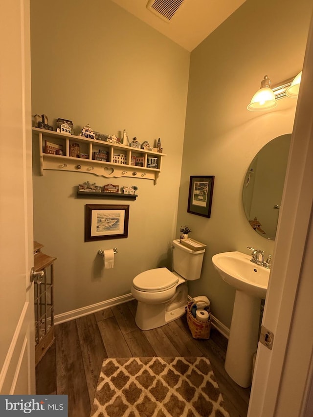 bathroom with visible vents, toilet, a sink, wood finished floors, and baseboards