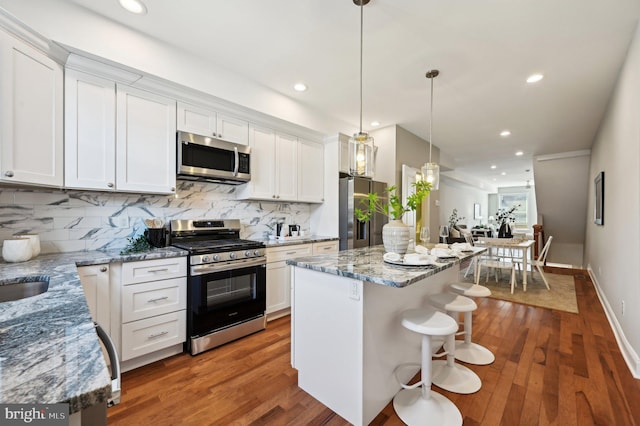 kitchen featuring a kitchen island, decorative backsplash, appliances with stainless steel finishes, wood finished floors, and white cabinetry