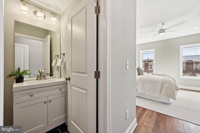 ensuite bathroom with baseboards, ceiling fan, vanity, hardwood / wood-style floors, and ensuite bath