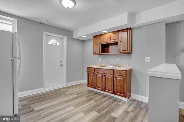 kitchen featuring light wood-style flooring, a sink, freestanding refrigerator, light countertops, and baseboards