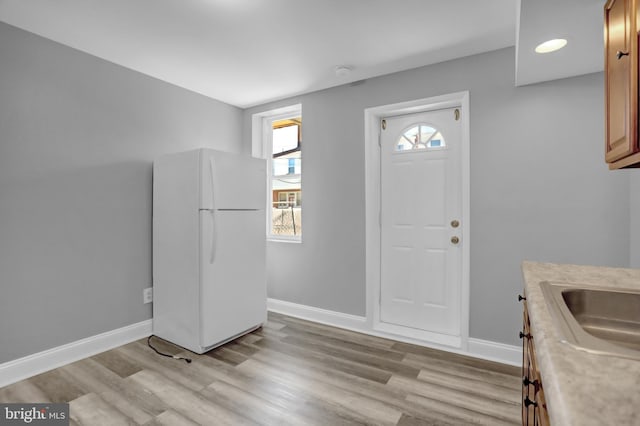 kitchen featuring a sink, freestanding refrigerator, light wood-style floors, light countertops, and baseboards