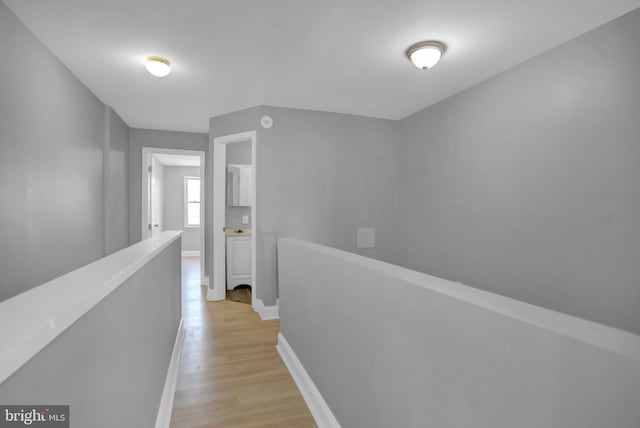 hallway with an upstairs landing, light wood-style flooring, and baseboards