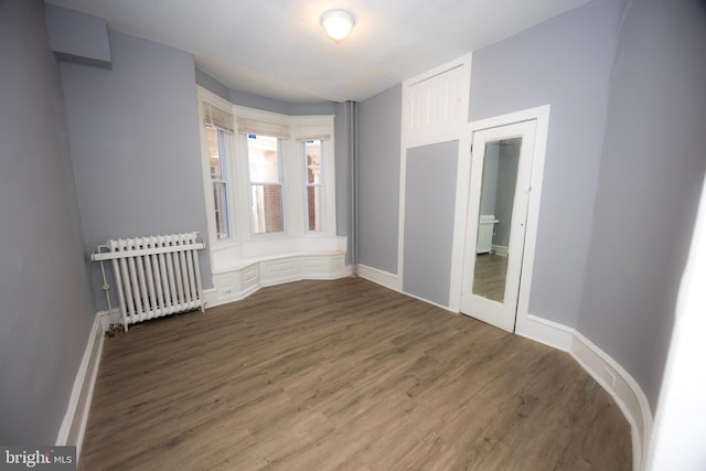 spare room with radiator heating unit, baseboards, and wood finished floors