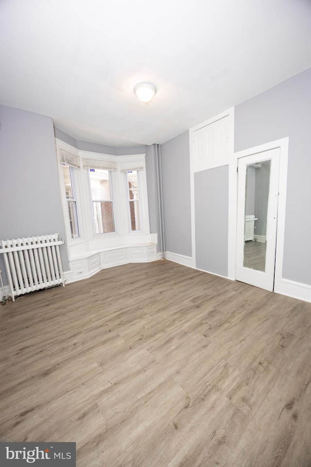 empty room with radiator, baseboards, and wood finished floors