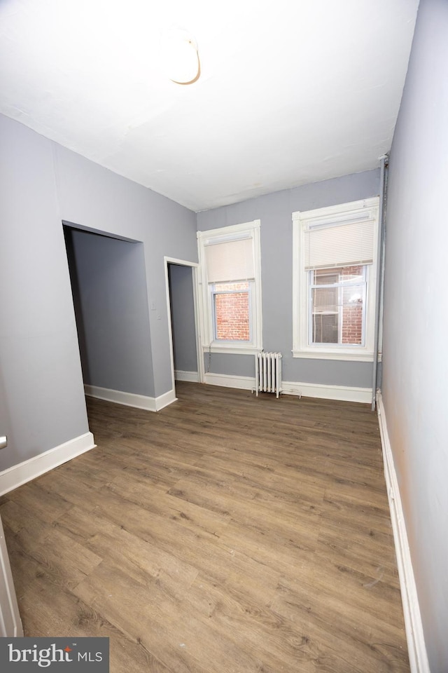 empty room featuring plenty of natural light, radiator heating unit, baseboards, and wood finished floors