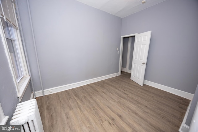 spare room with radiator, baseboards, and wood finished floors