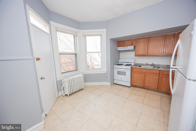 kitchen with tasteful backsplash, under cabinet range hood, radiator heating unit, brown cabinetry, and white appliances