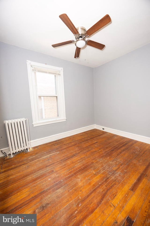 unfurnished room featuring baseboards, wood-type flooring, a ceiling fan, and radiator heating unit