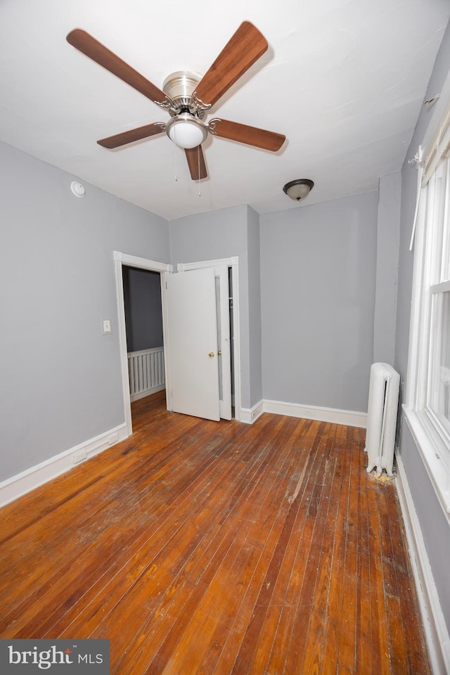 spare room with ceiling fan, baseboards, hardwood / wood-style floors, and radiator heating unit