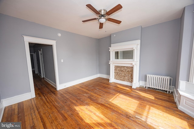 unfurnished living room featuring hardwood / wood-style floors, radiator, a ceiling fan, and baseboards