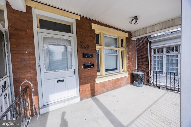 doorway to property featuring a porch and brick siding