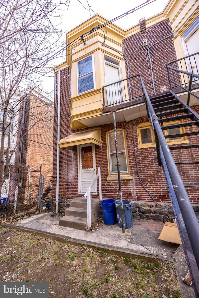 back of property featuring brick siding, a balcony, entry steps, and fence