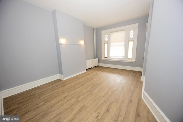 empty room with baseboards, radiator heating unit, and light wood finished floors